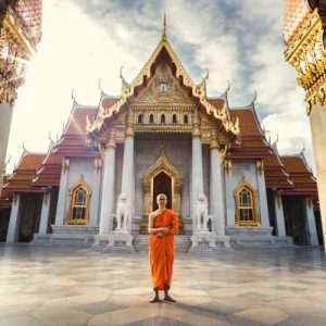 נזיר עומד יחף על רקע של מנזר בודהיסטי בבנקוק.