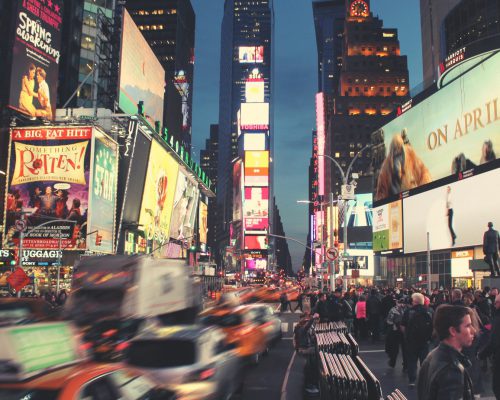 רחוב מלא באנשים ומסכי ענק המשדרות פרסומות בניו יורק.